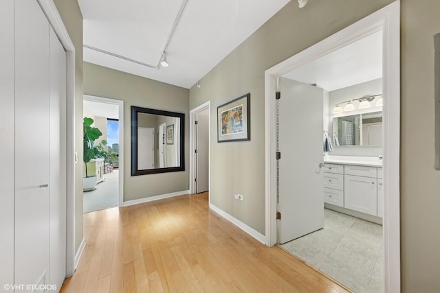 corridor featuring light wood-style floors, baseboards, and rail lighting