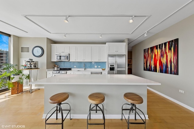 kitchen featuring stainless steel appliances, a sink, tasteful backsplash, a breakfast bar area, and baseboards