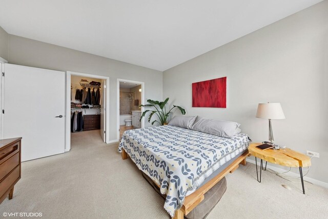 bedroom with light colored carpet, a spacious closet, a closet, baseboards, and ensuite bath