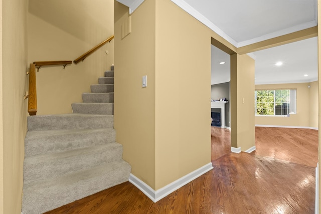 staircase with baseboards, a fireplace, crown molding, and wood finished floors