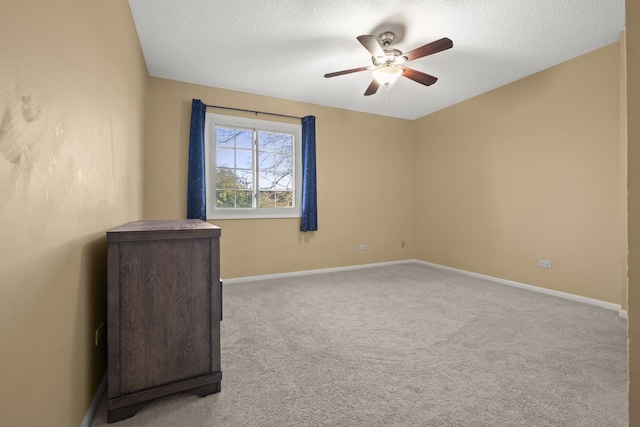 empty room with a ceiling fan, light colored carpet, a textured ceiling, and baseboards