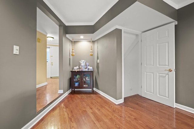 hallway with baseboards, ornamental molding, and light wood-type flooring