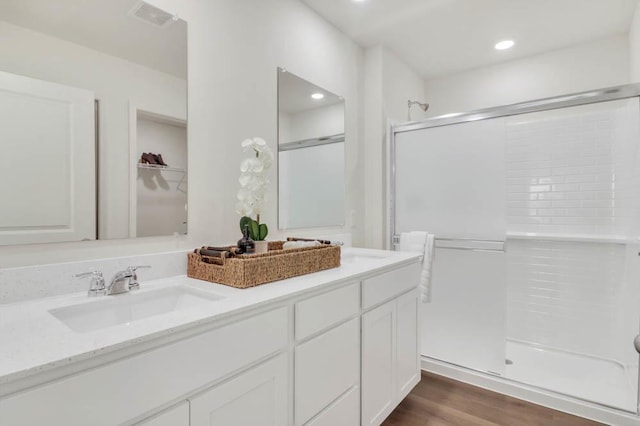 bathroom with a sink, wood finished floors, visible vents, a shower stall, and double vanity