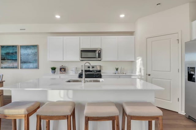 kitchen with a sink, a kitchen breakfast bar, white cabinets, appliances with stainless steel finishes, and dark wood-style floors