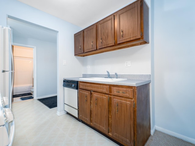 kitchen featuring freestanding refrigerator, dishwasher, baseboards, a sink, and light countertops