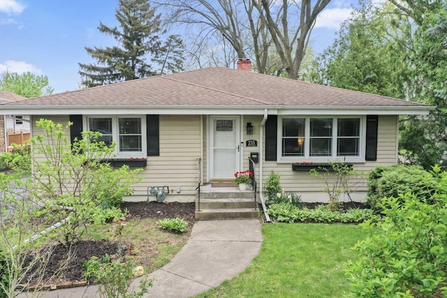 view of front facade with a chimney, a front yard, and a shingled roof