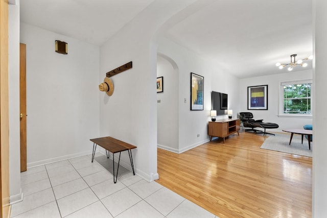 entryway with arched walkways, a chandelier, light wood finished floors, and baseboards