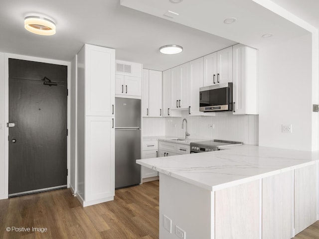 kitchen with a peninsula, wood finished floors, a sink, light stone countertops, and appliances with stainless steel finishes