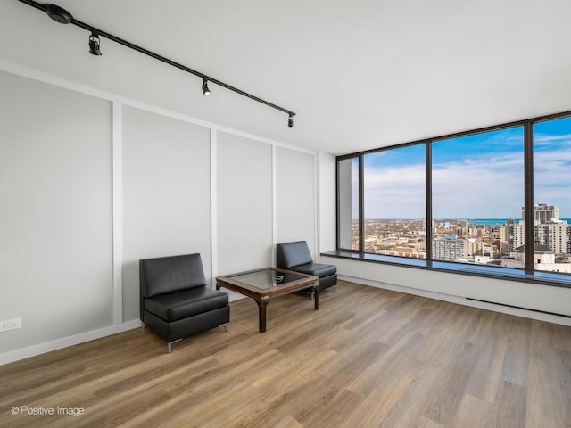 living area with a city view, rail lighting, wood finished floors, and baseboards