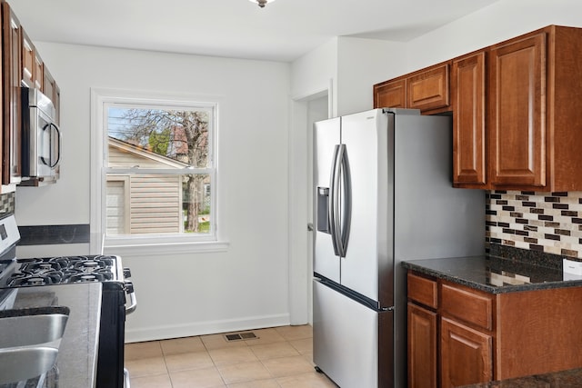 kitchen featuring appliances with stainless steel finishes, decorative backsplash, light tile patterned flooring, baseboards, and dark stone countertops