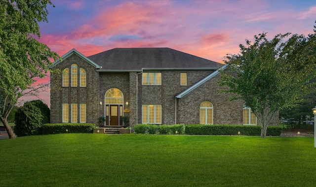 georgian-style home with a front yard, brick siding, and a shingled roof