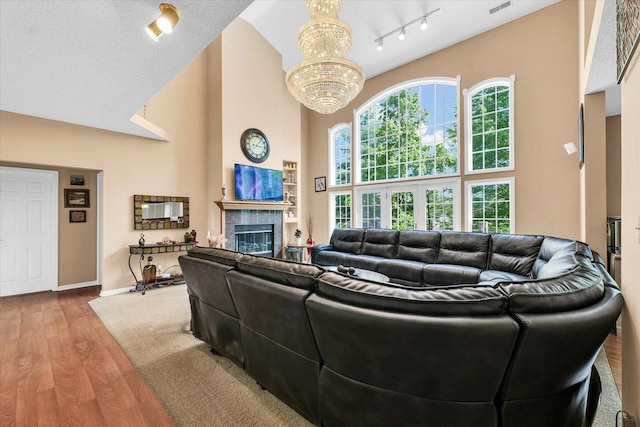 living room with a chandelier, a high ceiling, wood finished floors, a glass covered fireplace, and track lighting