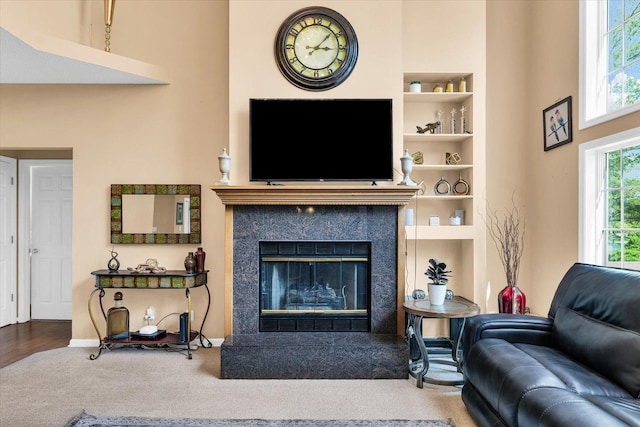 carpeted living area with a high end fireplace, built in shelves, and baseboards