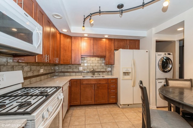 kitchen with light tile patterned floors, stacked washer and dryer, a sink, white appliances, and tasteful backsplash