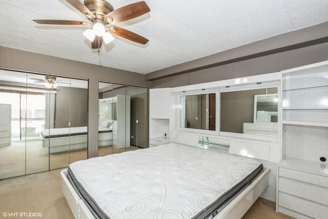 bedroom featuring two closets, light carpet, and a ceiling fan