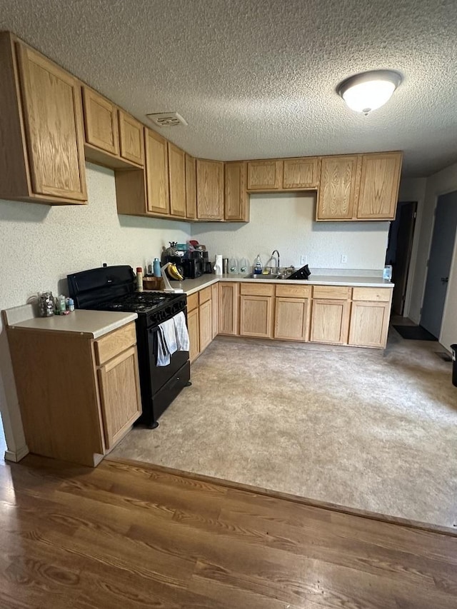 kitchen featuring wood finished floors, a sink, a textured ceiling, black gas stove, and light countertops
