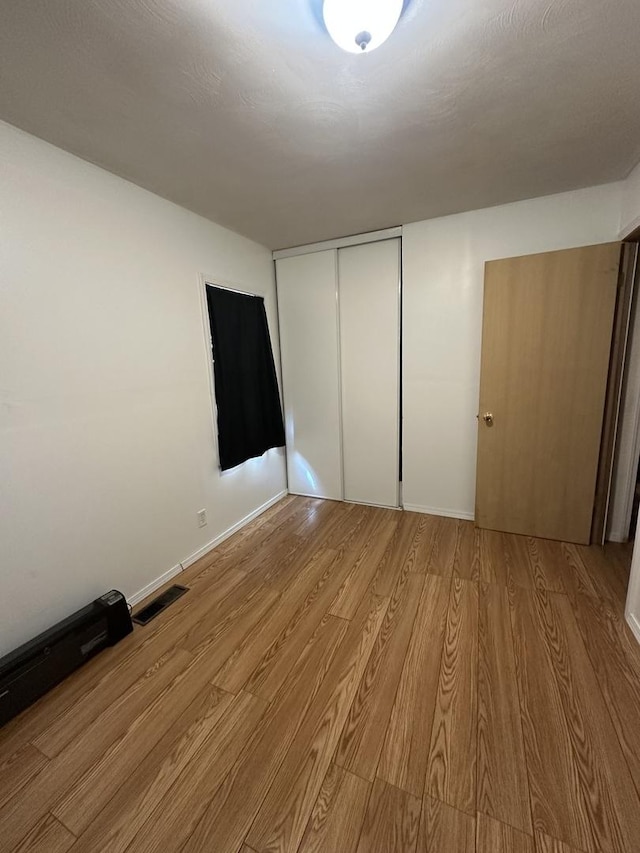 unfurnished bedroom featuring baseboards, a closet, light wood-style flooring, and visible vents