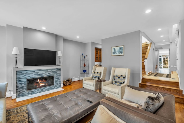 living area with stairs, a tiled fireplace, recessed lighting, and wood finished floors