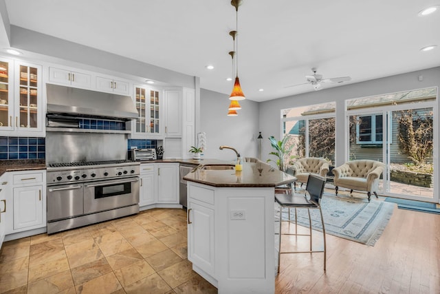 kitchen featuring a sink, a peninsula, stainless steel appliances, under cabinet range hood, and white cabinets