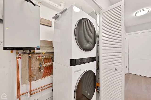 clothes washing area with laundry area, water heater, wood finished floors, and stacked washer and dryer