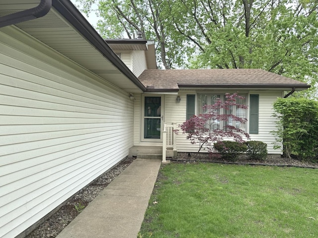 view of exterior entry with a shingled roof and a yard