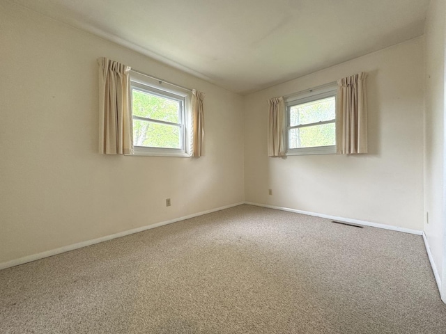 unfurnished room with carpet, a wealth of natural light, visible vents, and baseboards