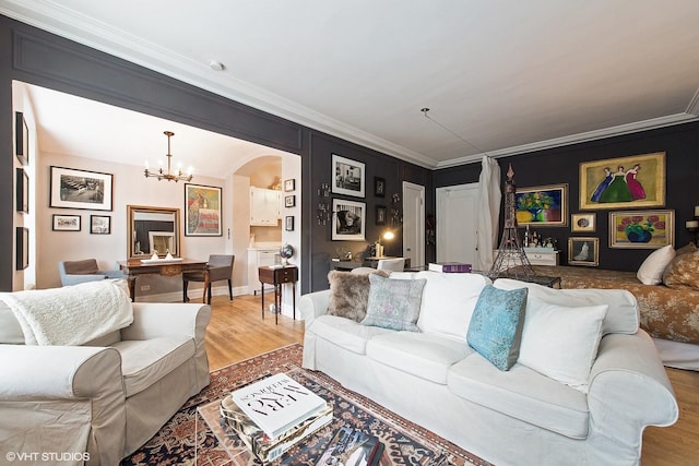 living room featuring arched walkways, ornamental molding, a chandelier, and light wood finished floors