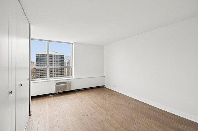 empty room with light wood-type flooring, baseboards, a city view, and a wall mounted air conditioner