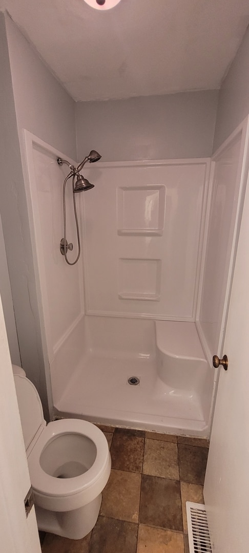 bathroom featuring toilet, visible vents, a stall shower, and stone finish floor