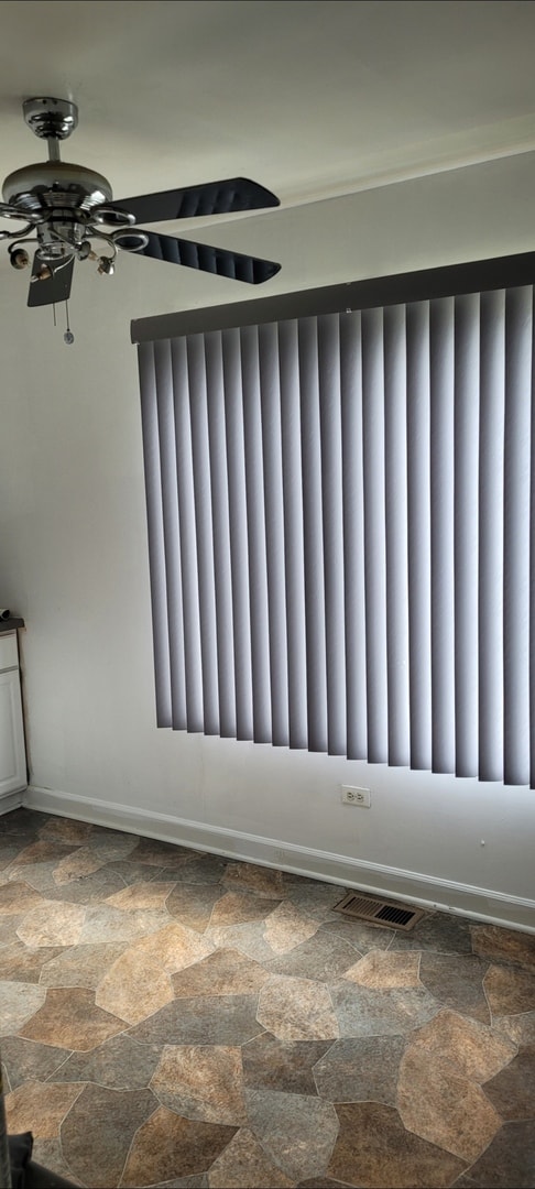 unfurnished room with stone tile flooring, a ceiling fan, and radiator heating unit