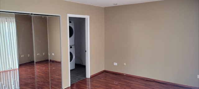unfurnished bedroom featuring a closet, stacked washing maching and dryer, wood finished floors, and baseboards