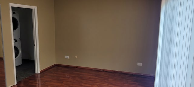 unfurnished bedroom featuring stacked washer / dryer, dark wood-type flooring, baseboards, and a walk in closet