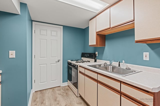 kitchen with gas range oven, a sink, light wood-style flooring, light countertops, and baseboards