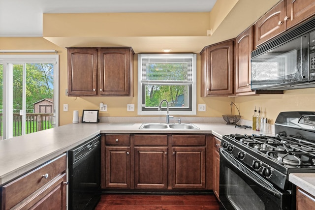 kitchen with black appliances, a sink, light countertops, and dark wood-type flooring