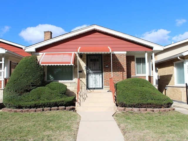 view of front of property featuring brick siding, a front lawn, and a chimney