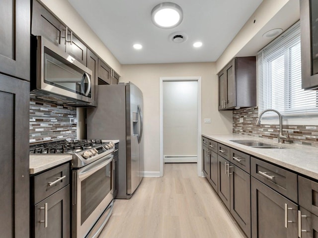 kitchen featuring a sink, stainless steel appliances, a baseboard heating unit, light wood finished floors, and light countertops