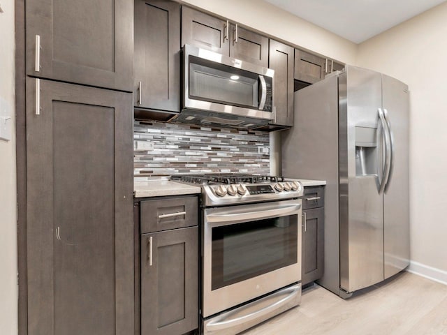 kitchen with light wood finished floors, baseboards, backsplash, light countertops, and appliances with stainless steel finishes