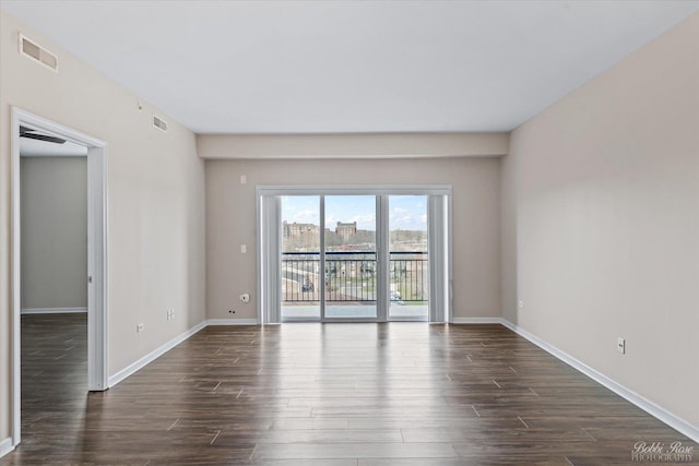 unfurnished room featuring visible vents, baseboards, and dark wood-style floors