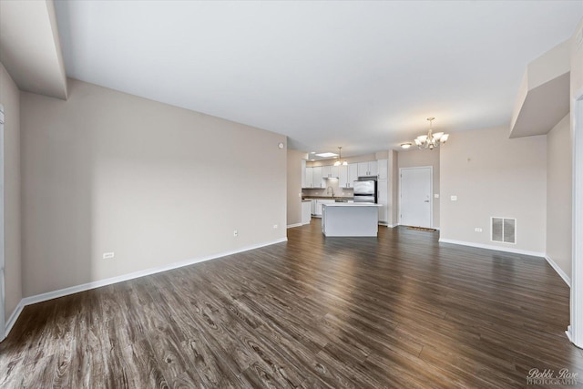 unfurnished living room with an inviting chandelier, dark wood-style flooring, baseboards, and visible vents