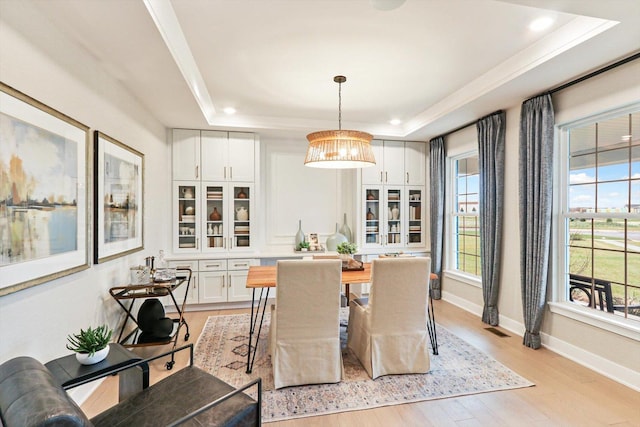 dining area featuring light wood-type flooring, visible vents, a chandelier, a raised ceiling, and baseboards