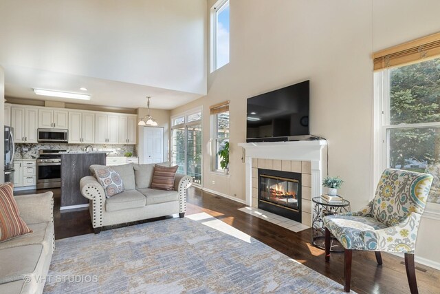 living room with wood finished floors, a tile fireplace, baseboards, and a high ceiling