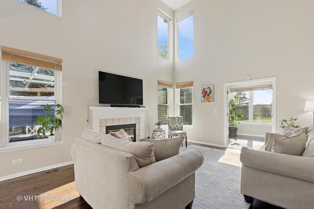 living area with a high ceiling, wood finished floors, baseboards, and a tiled fireplace