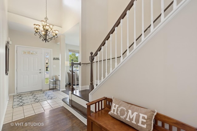 tiled foyer featuring a chandelier, a towering ceiling, stairway, and baseboards