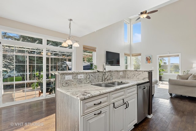 kitchen featuring open floor plan, stainless steel dishwasher, a sink, dark wood finished floors, and a towering ceiling