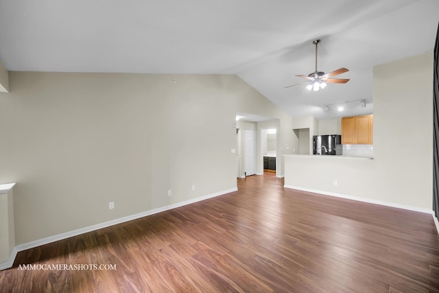 unfurnished living room with wood finished floors, rail lighting, baseboards, ceiling fan, and vaulted ceiling