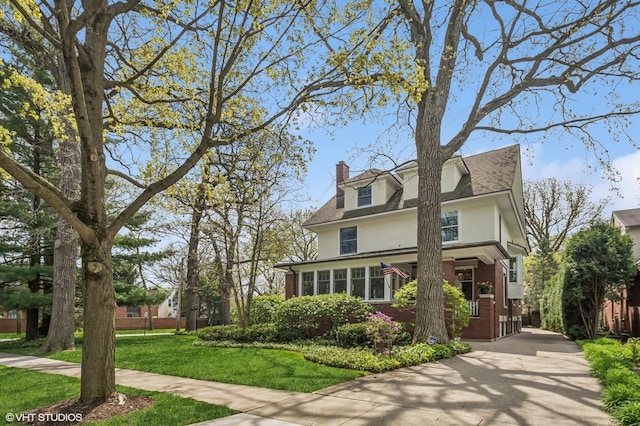 american foursquare style home featuring a chimney, stucco siding, a front lawn, brick siding, and concrete driveway