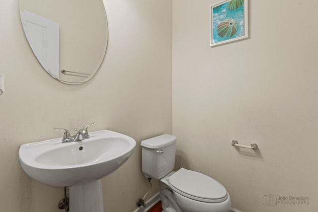 half bathroom with toilet, baseboards, and a sink