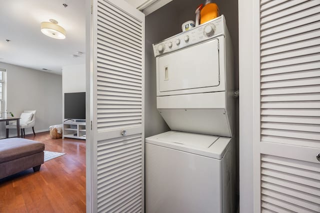 clothes washing area featuring laundry area, wood finished floors, baseboards, and stacked washer / drying machine