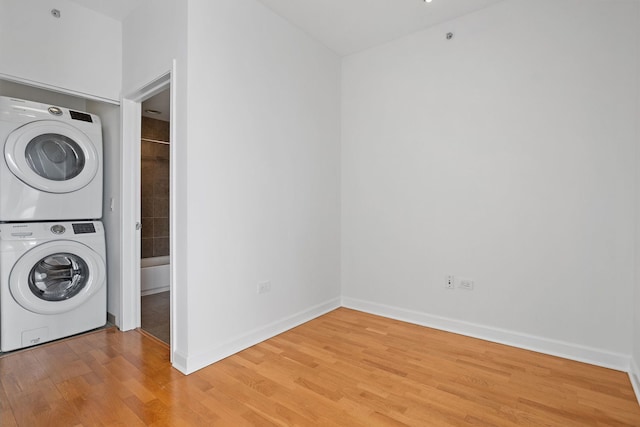 laundry room with estacked washer and dryer, light wood finished floors, and baseboards