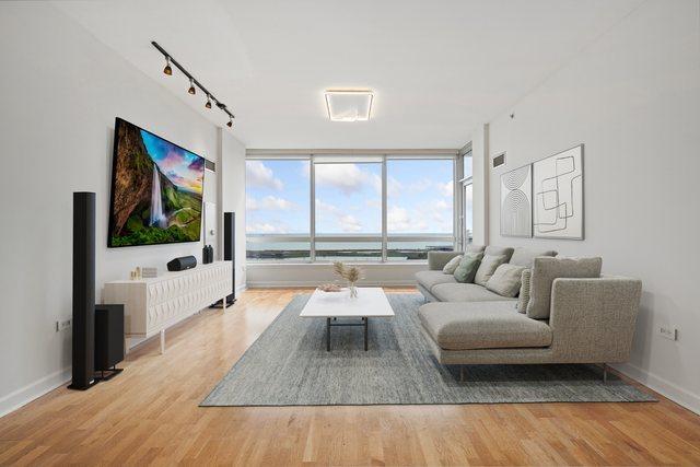 living room featuring rail lighting, wood finished floors, baseboards, and a wall of windows